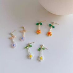 four pairs of colorful earrings sitting on top of a white table next to a cup