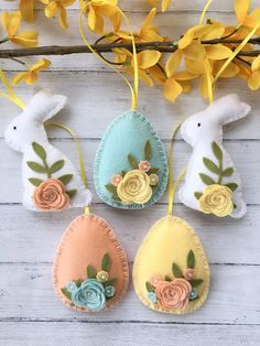 three easter eggs decorated with flowers and leaves on a white wooden surface next to yellow flowers