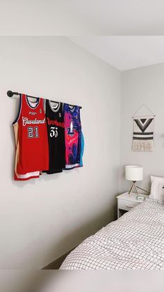 a bed room with a neatly made bed and three basketball jerseys hanging on the wall