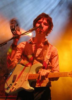 a young man playing an electric guitar in front of a microphone and stage lights at a concert