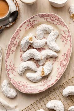 powdered doughnuts are arranged on a plate with coffee and spoons in the background