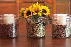 three jars with sunflowers and seeds in them on a table next to two candles