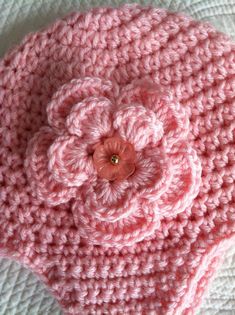 a pink crocheted hat with a flower on it sitting on top of a white blanket