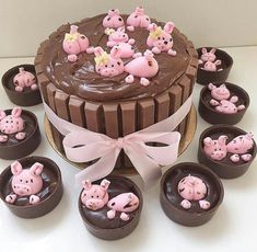 a chocolate cake with pink pigs on top surrounded by cupcakes and candies