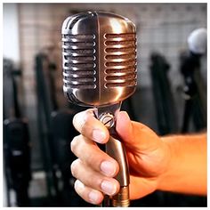 a hand holding a microphone in front of a brick wall with other equipment behind it