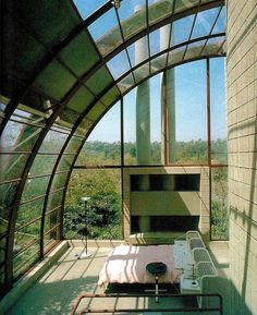 a bedroom with large windows and a bed in the middle, surrounded by greenery