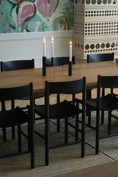 a dining room table with chairs and candles on the top, in front of a large painting