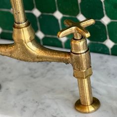 a gold faucet on a marble counter top in front of green tile backsplash