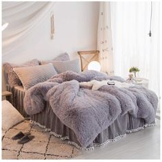 the bed is made up with fluffy grey blankets and pillows on top of it,