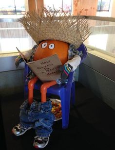 an orange sitting on top of a blue chair with a straw hat on it's head