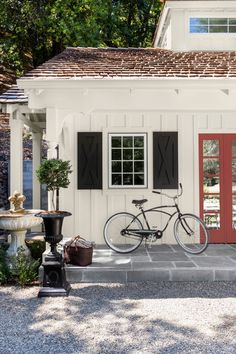 a bicycle is parked in front of a white house with red doors and shutters