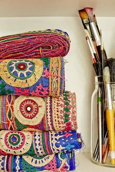 a stack of colorful cloths and brushes next to a vase filled with paintbrushes