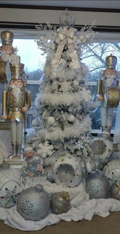 a white christmas tree in front of a window with lots of silver ornaments on it