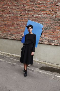 a woman standing on the street holding a blue piece of paper