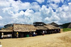 people are standing in front of thatched huts on the side of a dirt road