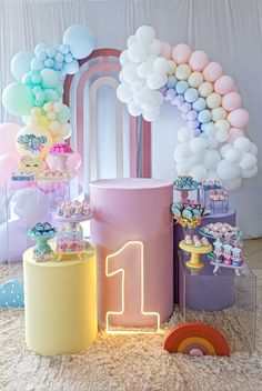 a birthday party with balloons and decorations on the floor in front of a rainbow arch