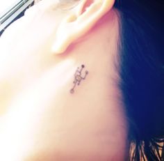 a woman's ear with a small cross tattoo on her left behind the ear