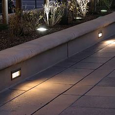 some lights that are on the side of a wall near a sidewalk and trees at night