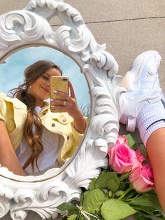 a woman taking a selfie in front of a mirror with flowers on the ground