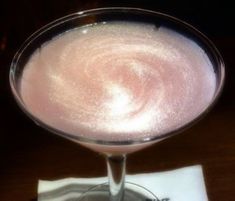 a drink in a coupe glass on top of a white napkin with pink flecks