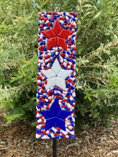 a red, white and blue glass star decoration on a stake in front of some bushes