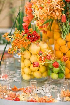 an arrangement of flowers and fruit in vases on a table with other items around it