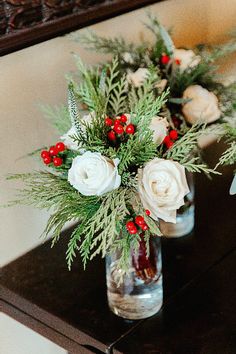 two vases filled with flowers and greenery on top of a wooden table next to a mirror