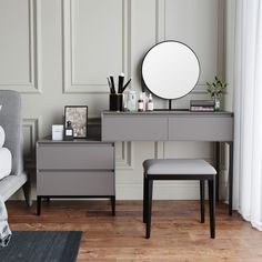 a gray dresser with a mirror, stool and other items on the table in front of it