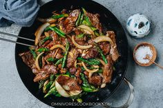 beef and asparagus stir fry in a wok with garlic on the side