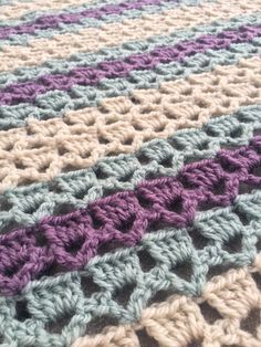 a crocheted blanket is laying on top of a tablecloth with purple and white stripes