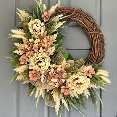 a wreath is hanging on the front door with dried flowers and greenery around it