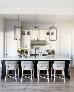 a large kitchen with white cabinets and black island in the center is surrounded by four stools