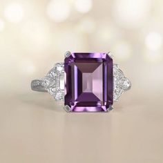 A Stunning Vivid Gemstone Ring Features A 6.32 Carat, Emerald Cut, Natural Amethyst Center Stone. Luxury Amethyst Ring Emerald Cut, Luxury Purple Amethyst Ring, Rectangular Shape, Luxury Emerald Cut Amethyst Ring, Elegant Purple Amethyst Baguette Cut Ring, Luxury Purple Amethyst Rectangular Ring, Elegant Purple Baguette Cut Amethyst Ring, Luxury Purple Rectangular Amethyst Ring, Elegant Emerald Cut Amethyst Ring, Purple Amethyst Ring With Emerald Cut And Gemstone Accents