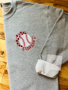 a t - shirt with a baseball embroidered on the front and back, sitting on a wooden floor