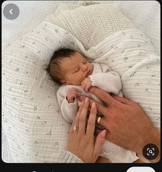 a man holding a baby in his arms while laying on top of a white blanket