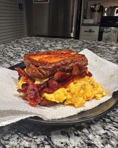 a breakfast sandwich with bacon, eggs and toast on a plate at the kitchen counter