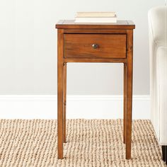 an end table with a book on top and a white chair in the back ground