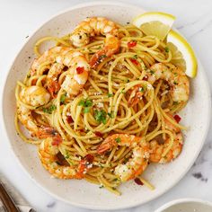 a white plate topped with pasta and shrimp next to lemon wedges on a marble table