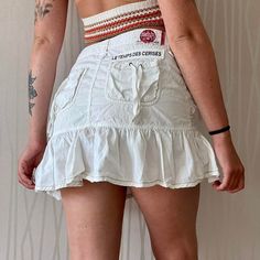 The adorable cargo miniskirt from brand Les Temps Des Cerises in the late 90's / early 2000's! Such a cute and flirty summer staple with the best detailing!  Features midweight 100% cotton construction, mid- low waist fit, drop waist affect, ruffle hem detail, tie up details on the front and back pockets, brand patch on the back waist band and above the pocket, white colorway and mini length! Tagged size 27, fits like a medium This piece has very light general wear and tear Y2k Mini Cargo Skirt For Spring, Y2k Style Mini Cargo Skirt For Spring, Y2k Mini Cotton Skort, Spring Y2k Mini Cargo Skirt, Y2k Style Fitted Skort With Ruffles, Y2k Fitted Skort With Ruffles, Y2k Style Mini Skort With Ruffles, Y2k Style Ruffled Skort, Y2k Fitted Ruffled Skort