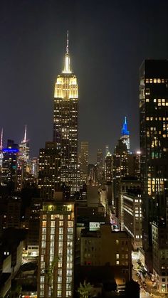 the empire building is lit up at night in new york city, with other skyscrapers visible