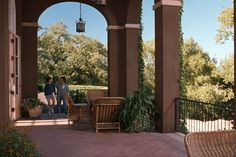 two people are standing on the patio with chairs and tables in front of an archway