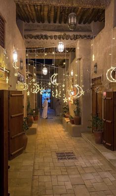 a narrow hallway with lights hanging from the ceiling and potted plants on either side