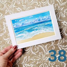 a person holding up a painting with the number thirty nine in front of it and an image of a beach