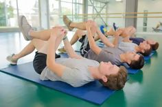 several people are doing exercises on mats in a gym together, one man is stretching and the other has his leg up