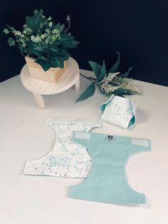 three baby bibs sitting on top of a table next to a potted plant