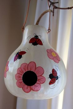 a white vase with pink flowers and ladybugs on it hanging from a branch