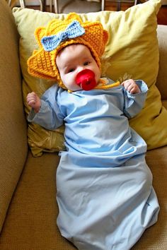 a baby in a blue dress and hat laying on a couch with a red nose