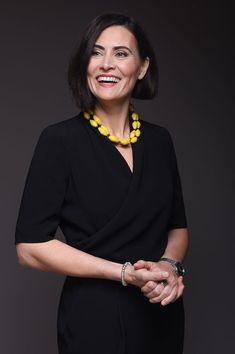 a woman in a black dress with a yellow necklace on her neck smiling at the camera