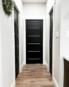 an empty hallway with black doors and wood flooring on the side walk between two white walls