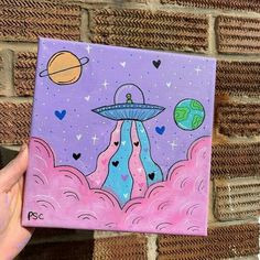 a hand holding up a painting on a brick wall with the image of an alien ship floating in space